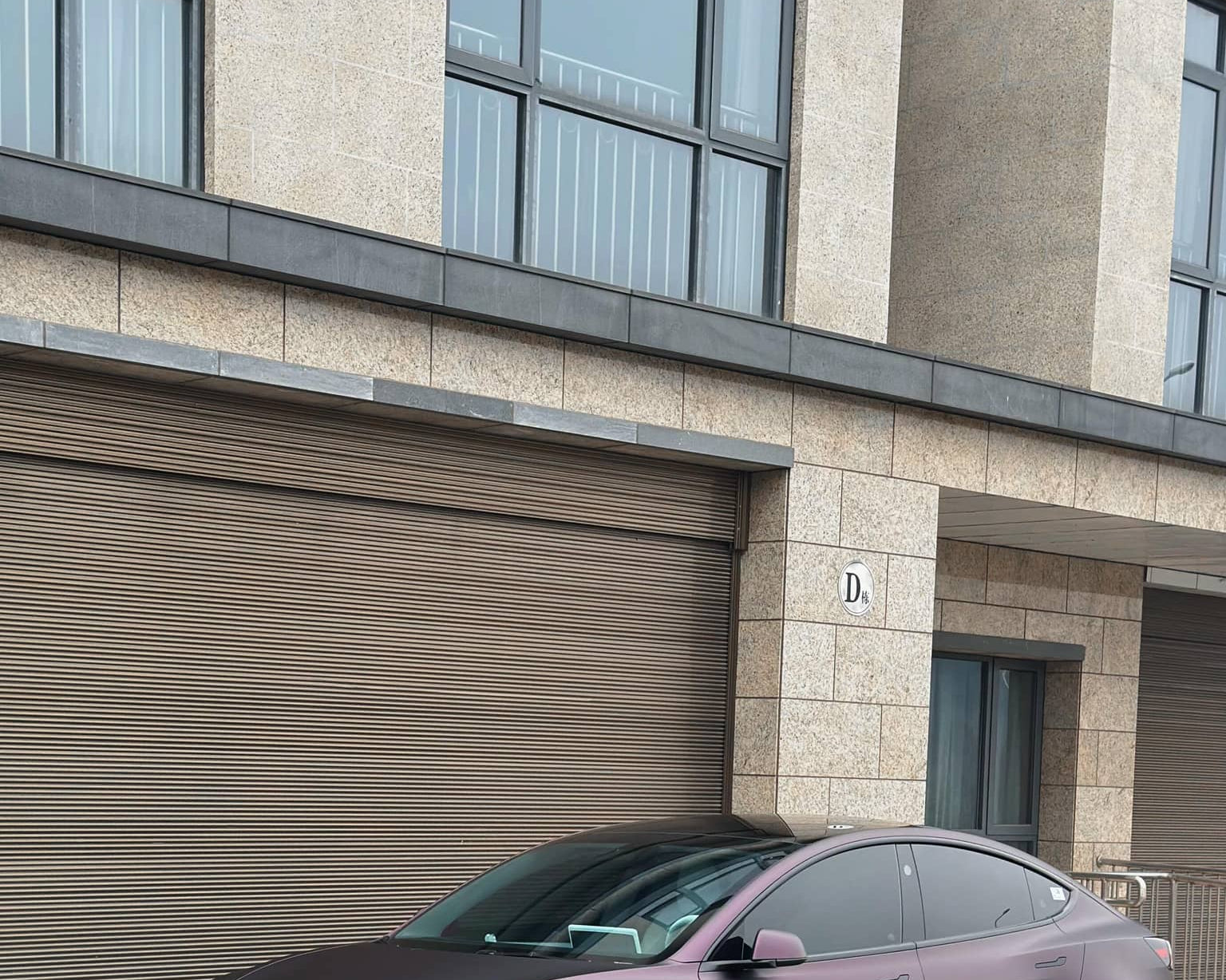 WrapBug matte purple Tesla Model 3 parked in front of a modern garage with black rims