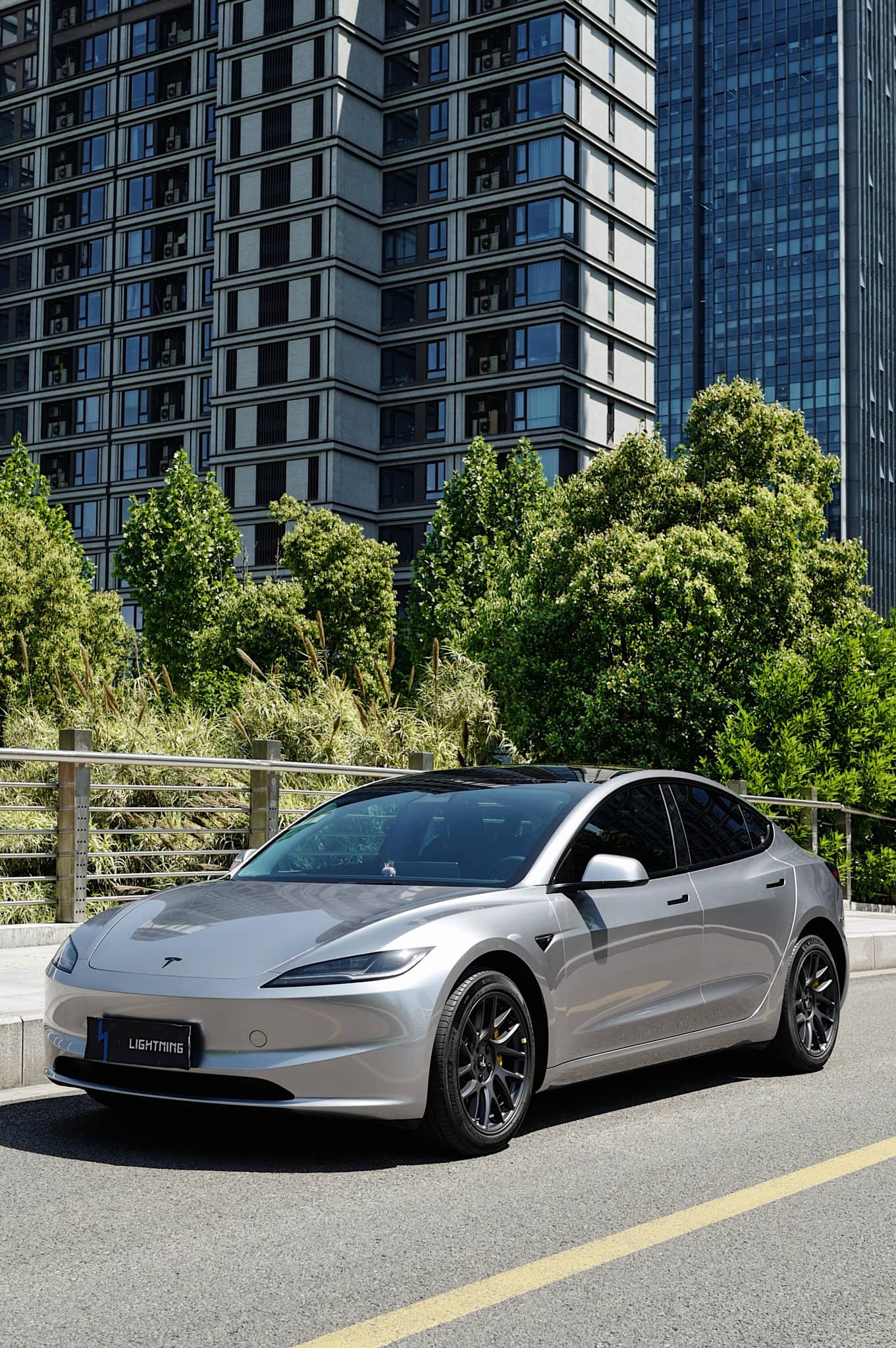 Silver Tesla Model 3 with black wheels parked on city street featuring WrapBug Pre-cut Tesla Wrap Kit