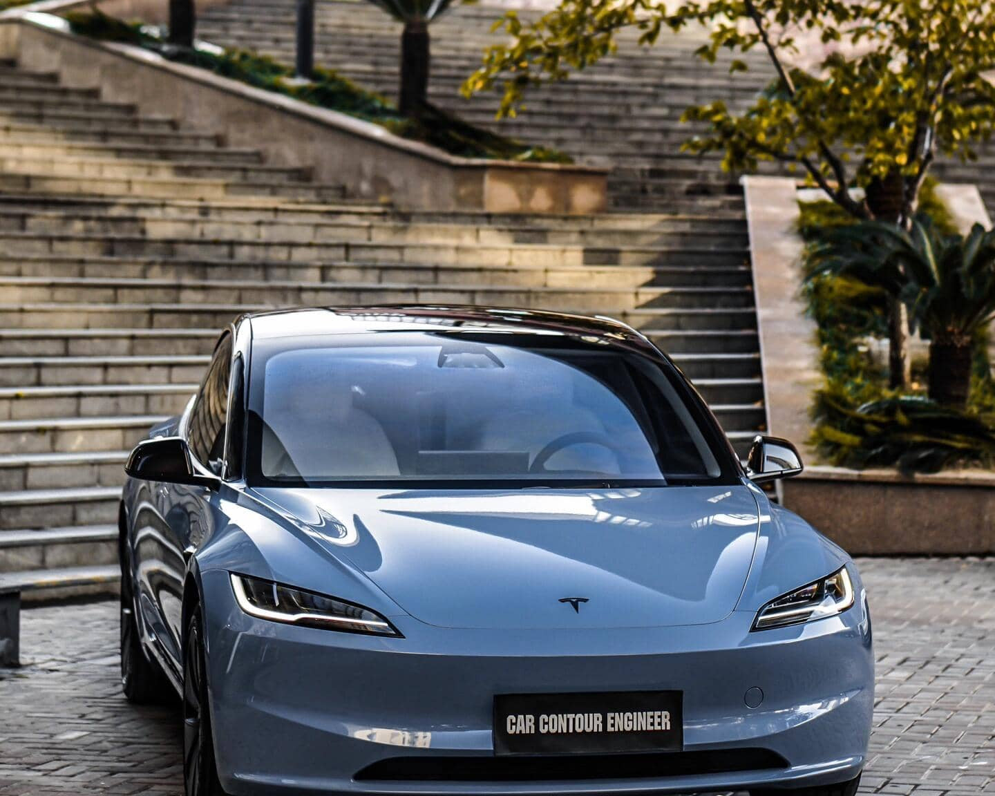Pre-cut Tesla Vinyl Wrap Kit applied on sleek blue Tesla parked near stone stairs and greenery
