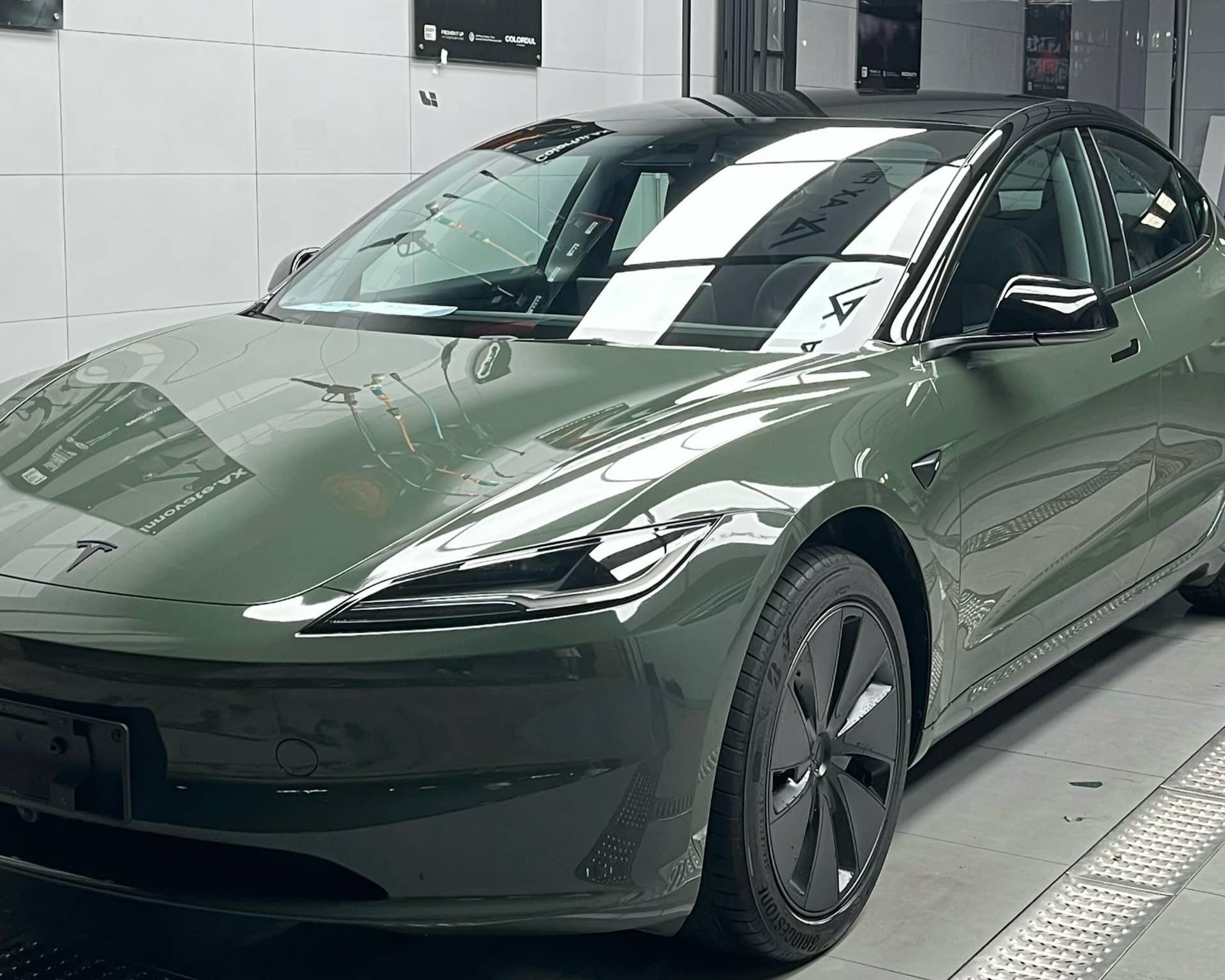 Green matte finish Tesla Model 3 electric car parked indoors with sleek aerodynamic design
