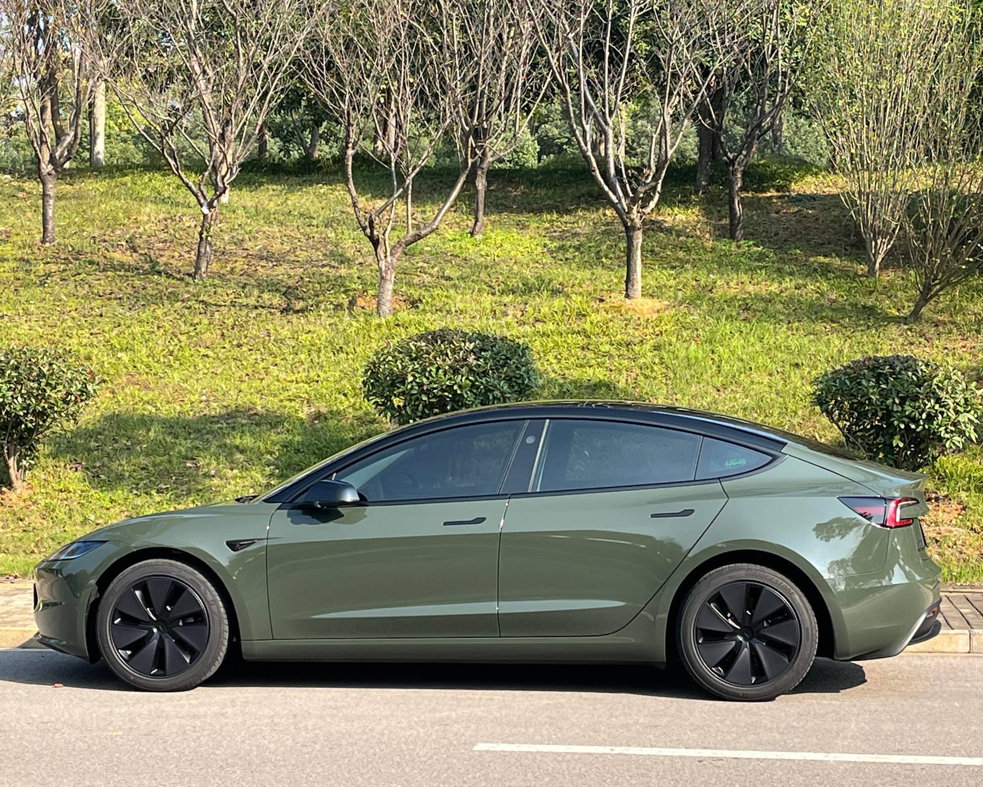 WrapBug olive green car wrap applied on a Tesla Model 3 parked on the street