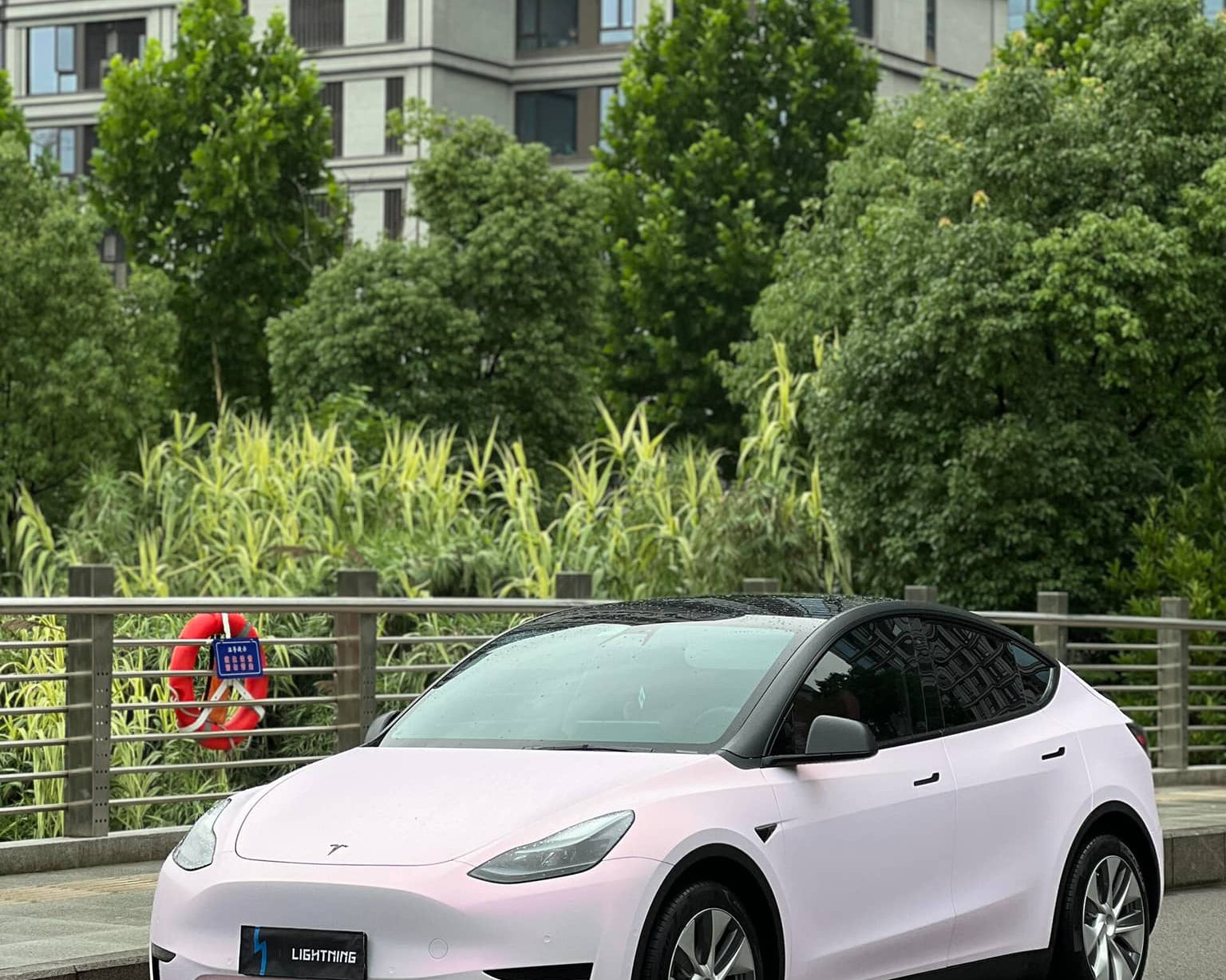 WrapBug pink Tesla Model Y electric car parked on city street near greenery and buildings