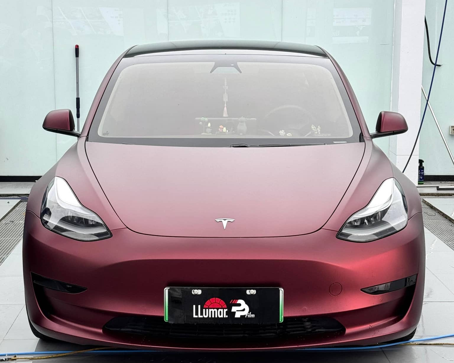 Front view of a matte maroon Tesla Model 3 electric car with sleek aerodynamic design