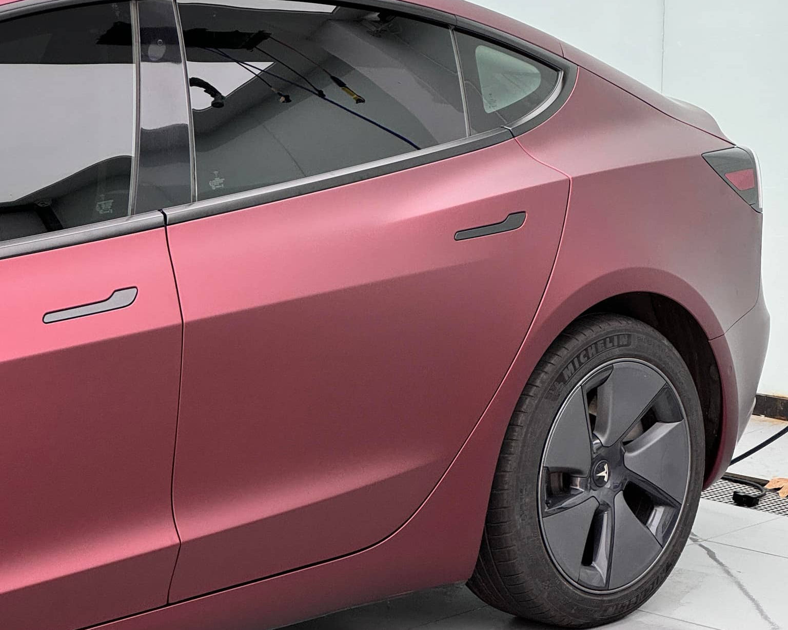 WrapBug matte burgundy car wrap on a Tesla Model 3 parked indoors with black rims