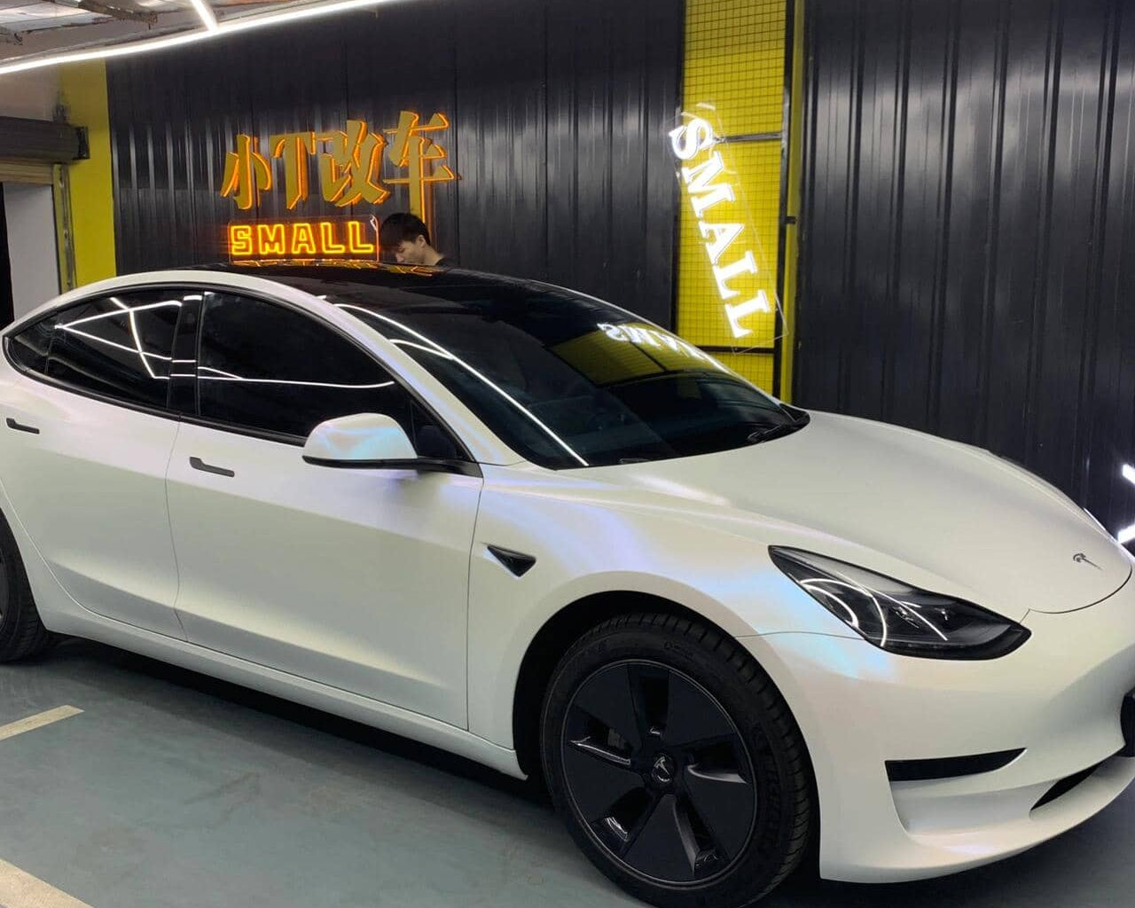 White Tesla Model 3 with matte white tesla wrap parked indoors under bright lighting