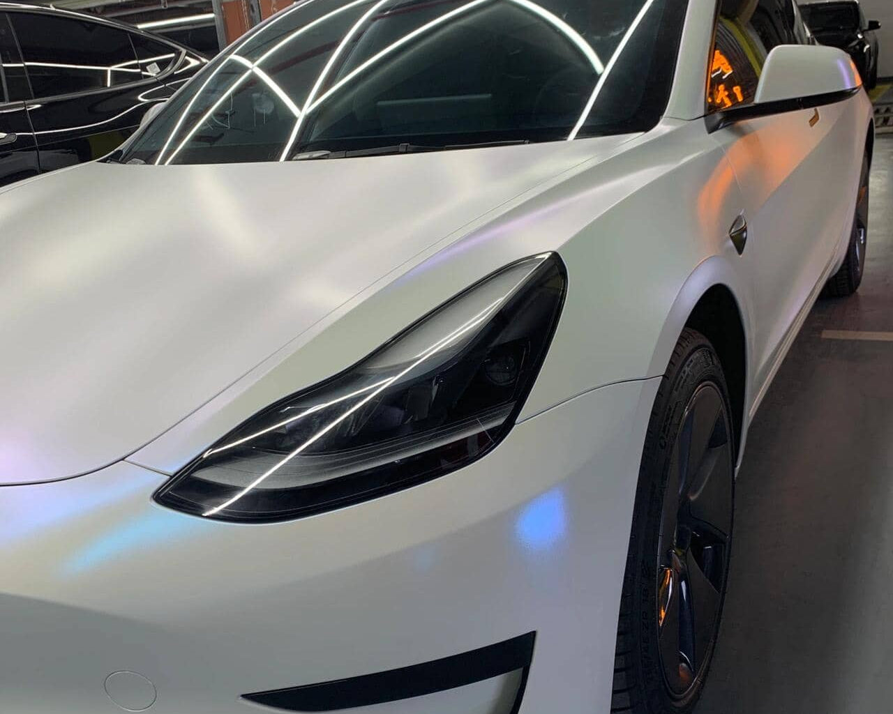 Tesla Model 3 with sleek matte white tesla wrap by WrapBug in a modern garage setting