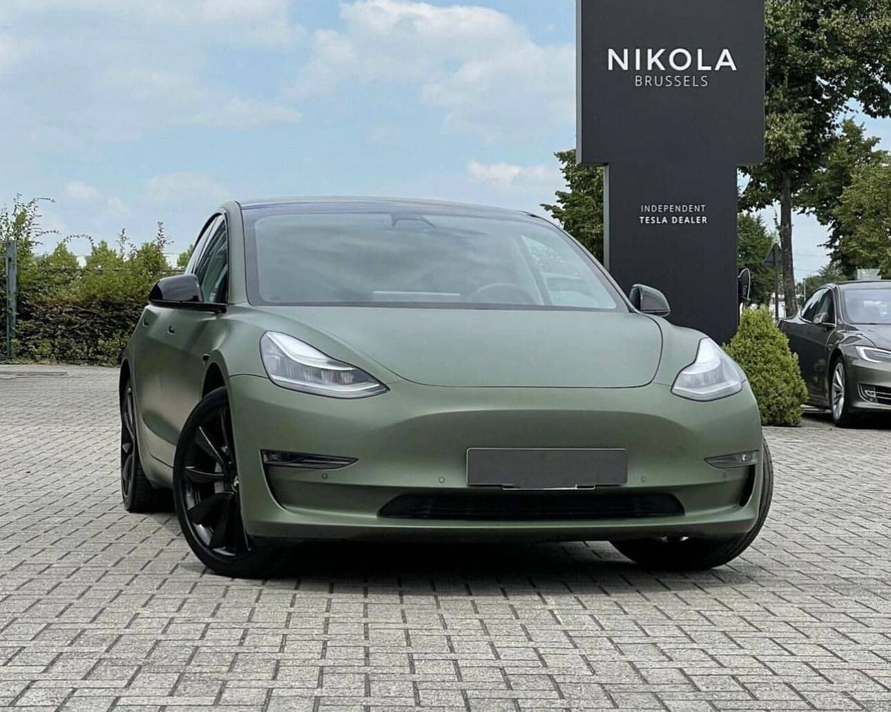 Matte green Tesla Model 3 with black wheels parked in front of Nikola Brussels Tesla dealer