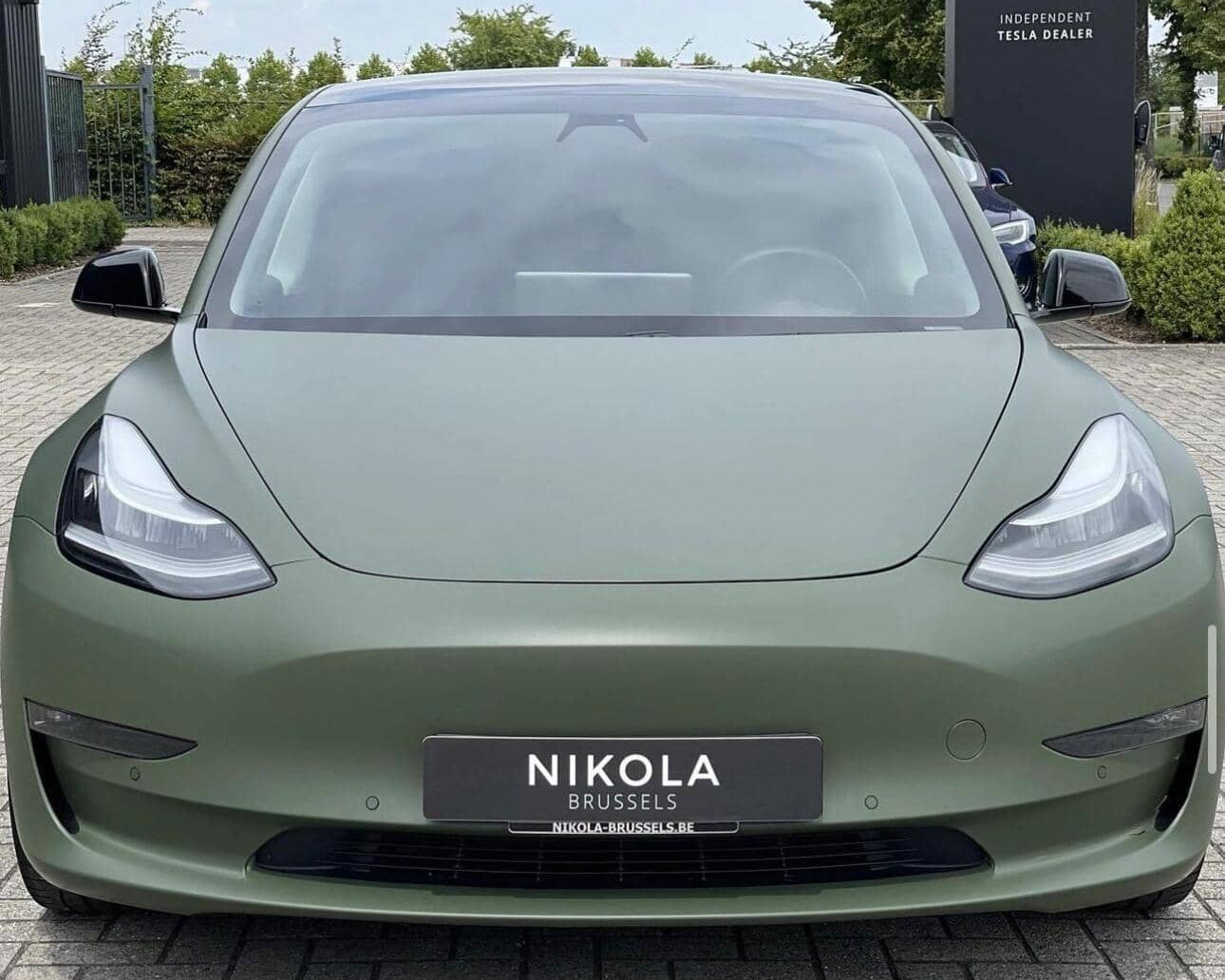 Matte green Tesla Model 3 electric car front view parked outside Nikola Brussels dealership