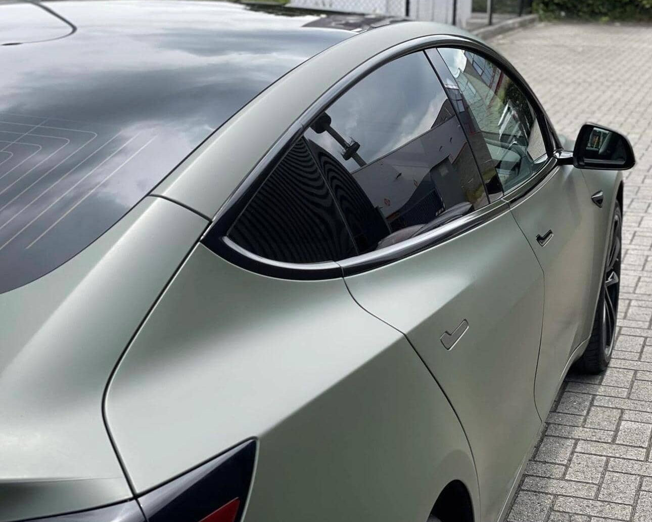 Gray Tesla Model 3 electric car parked on driveway showing rear side and tinted windows