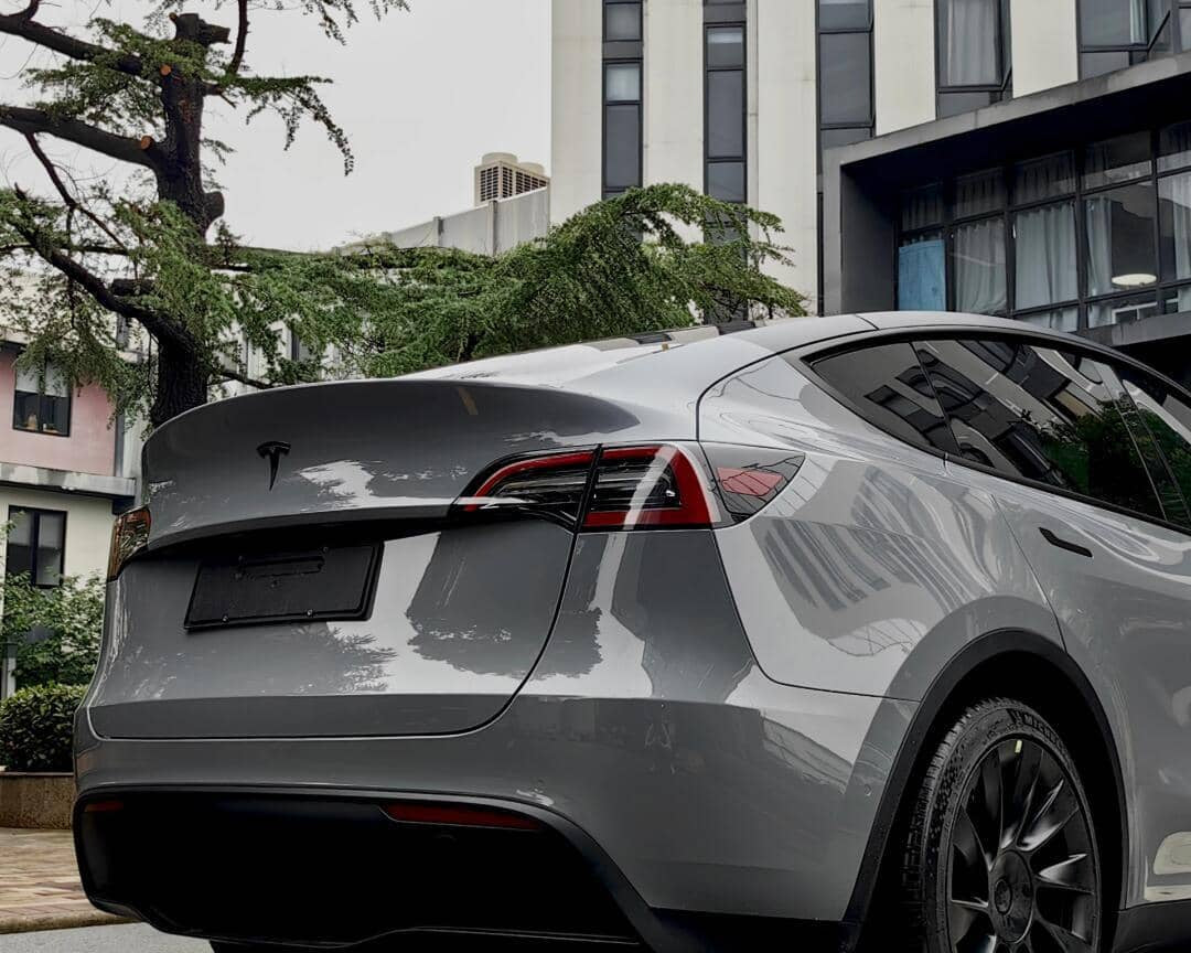 Gray Tesla Model Y parked near buildings showcasing Pre-cut Tesla Vinyl Wrap Kit application on the rear and side