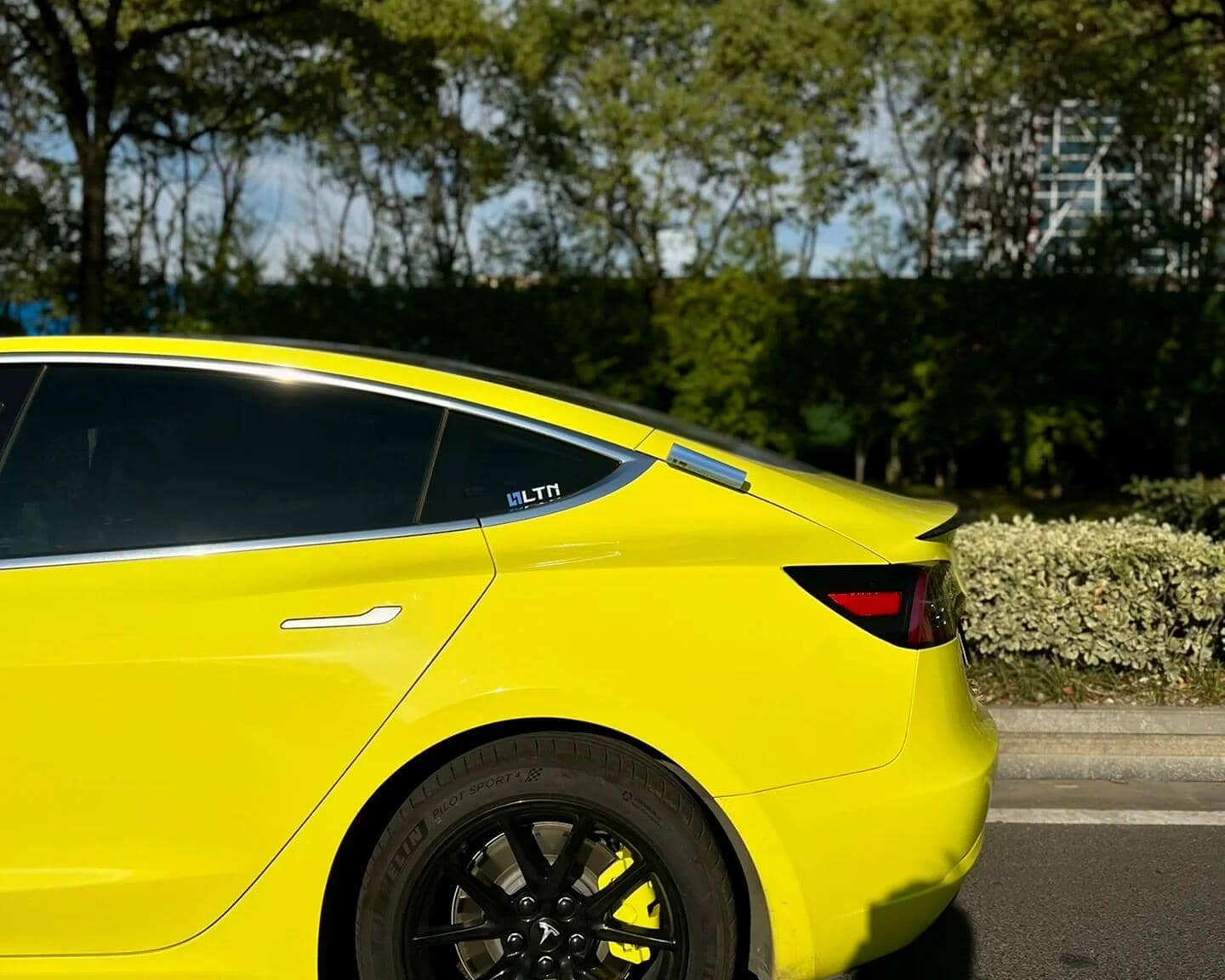 Yellow Tesla Model 3 wrapped using Pre-cut Tesla Vinyl Wrap Kit by WrapBug with black wheels in outdoor setting