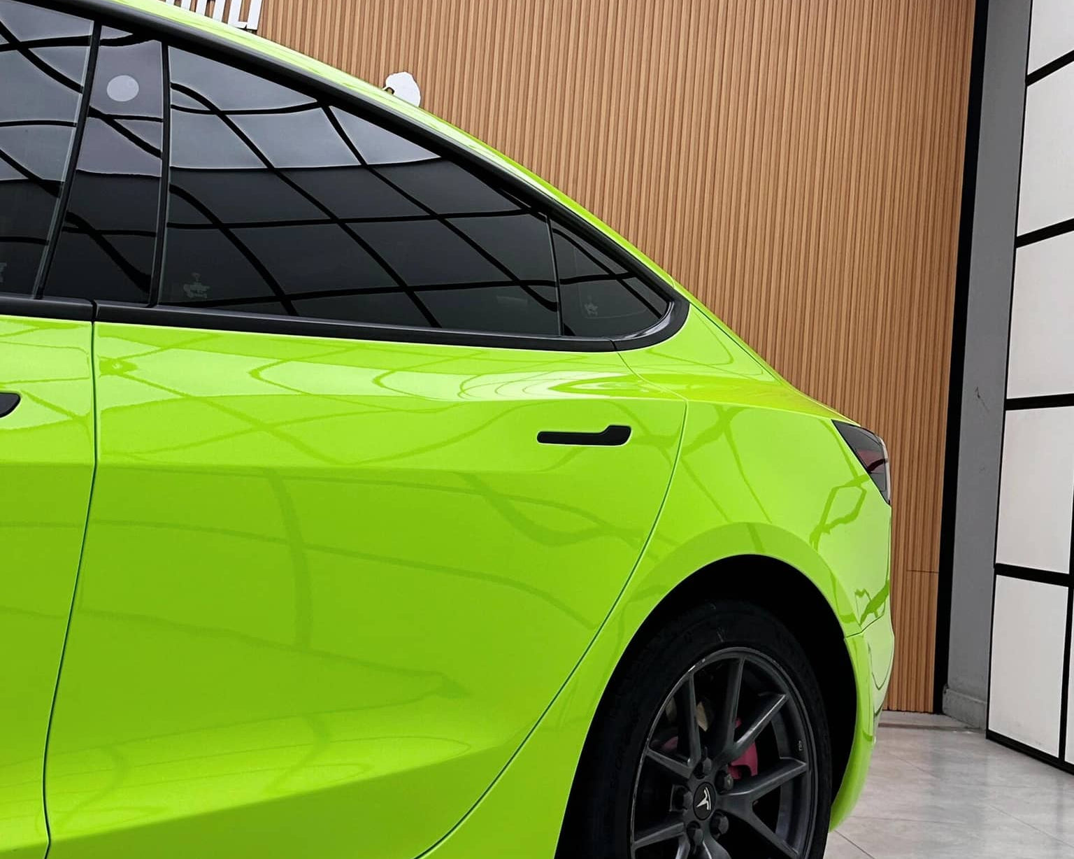 Bright green Tesla Model 3 wrapped with a Pre-cut Tesla Wrap Kit showing rear side view in a modern garage