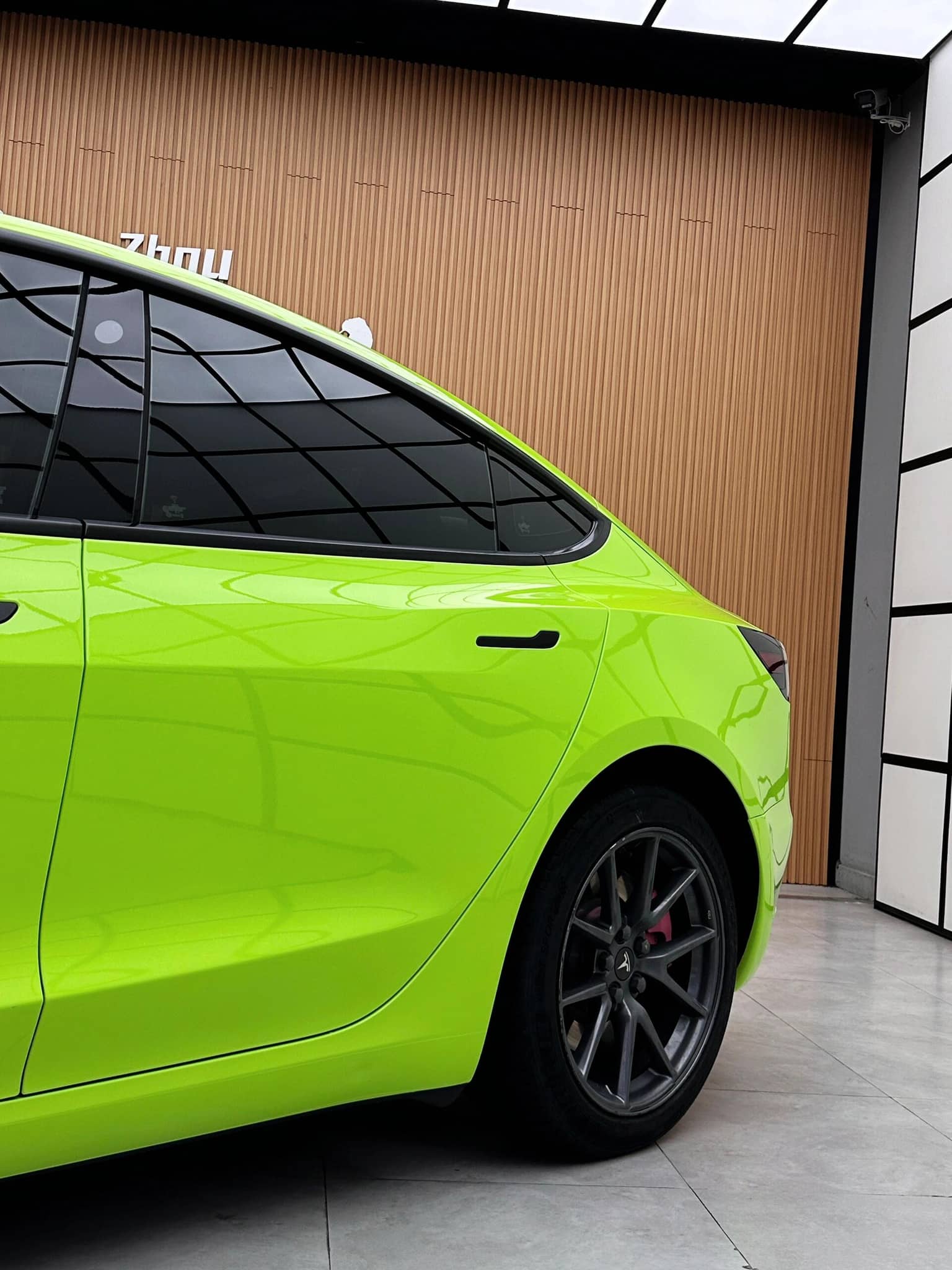 Bright green Tesla Model 3 wrapped with a Pre-cut Tesla Wrap Kit showing rear side view in a modern garage