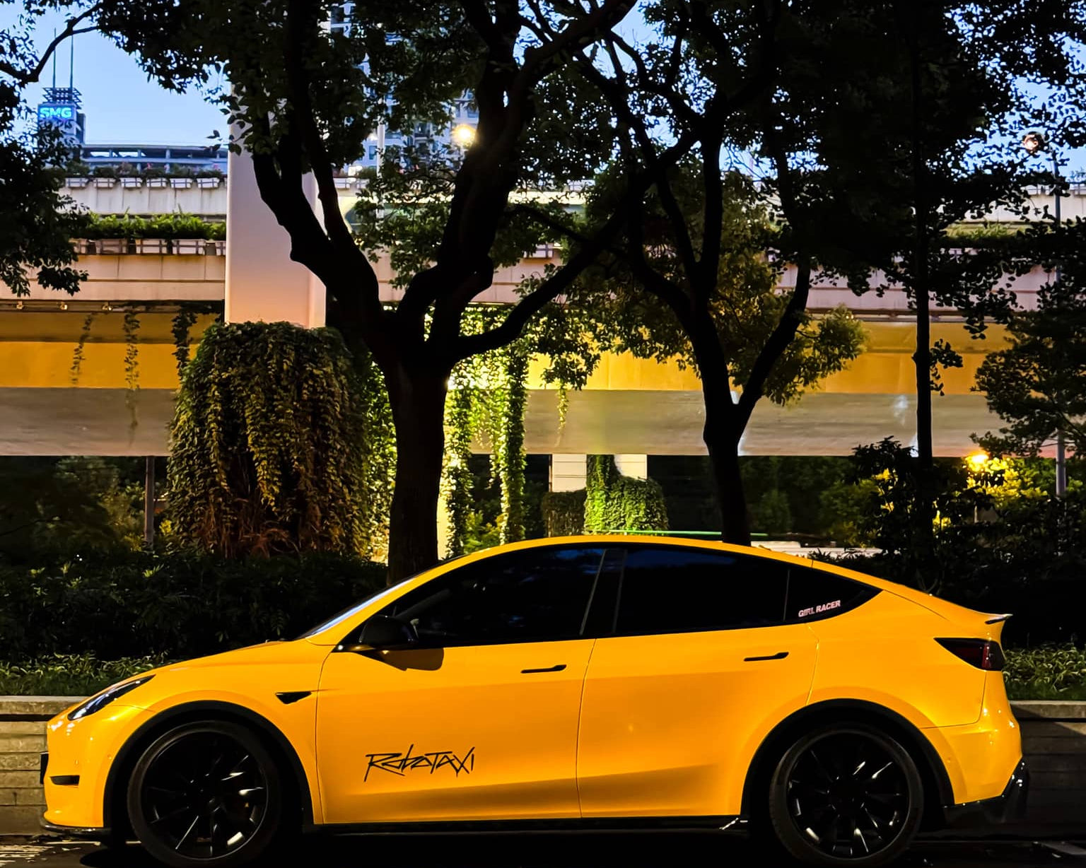 Yellow Tesla Model Y wrapped using Pre-cut Tesla Wrap Kit by WrapBug parked at night under trees