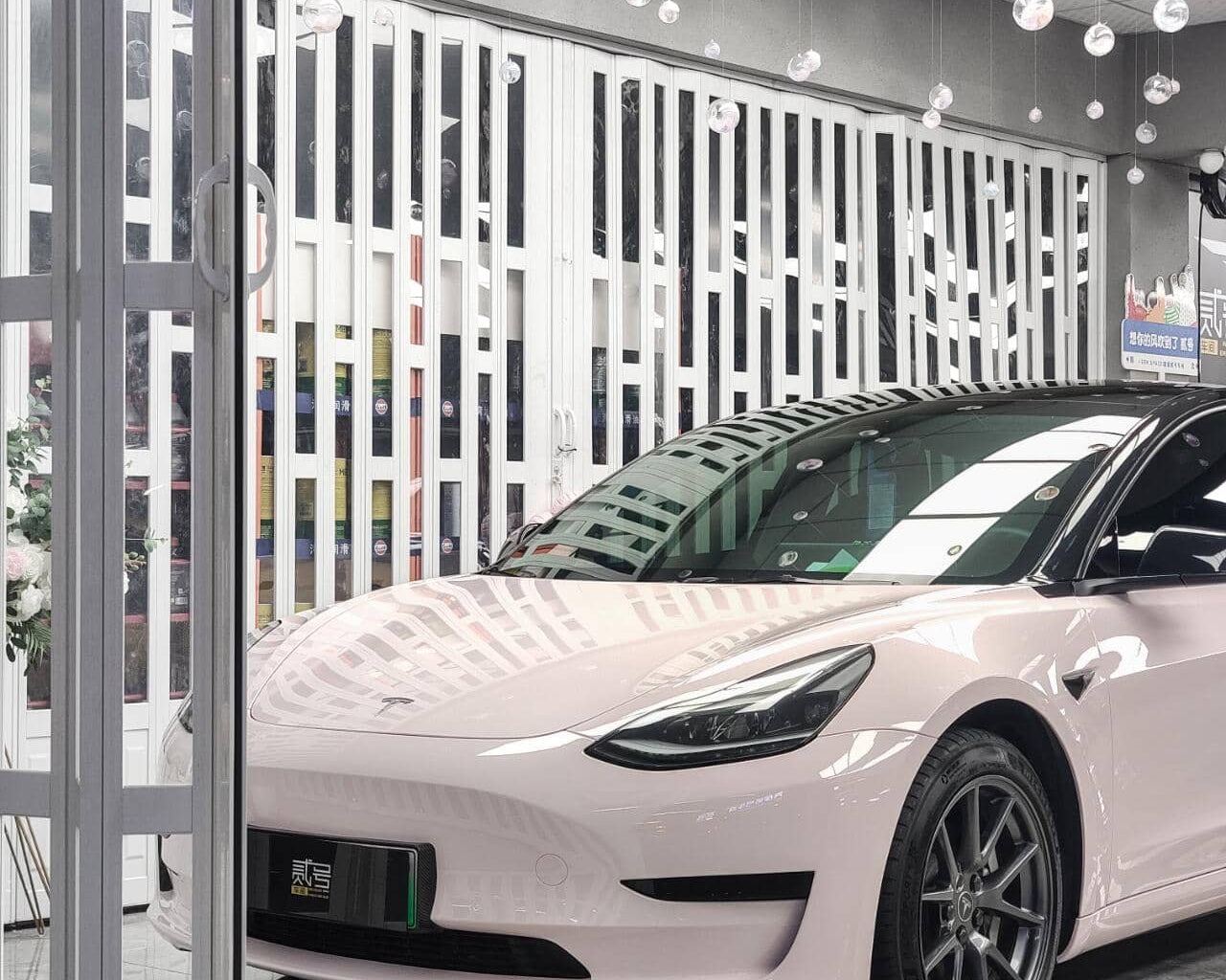 Tesla Model 3 with a glossy pink finish using WrapBug Pre-cut Tesla Wrap Kit in a modern garage