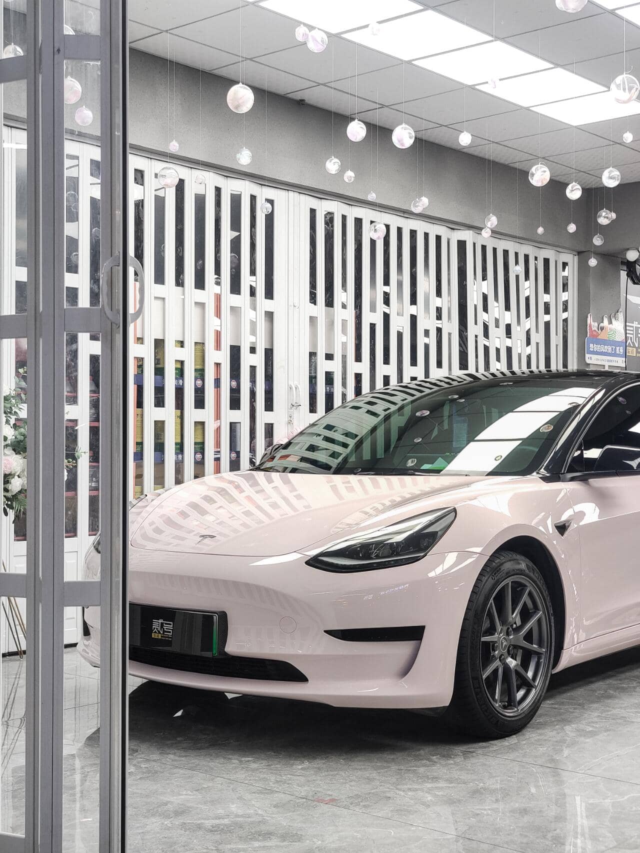 Tesla Model 3 with a glossy pink finish using WrapBug Pre-cut Tesla Wrap Kit in a modern garage