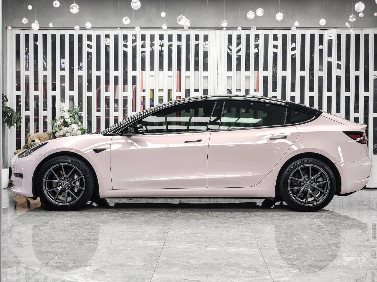 Tesla Model 3 with a smooth pink finish using WrapBug Pre-cut Tesla Wrap Kit in a modern showroom