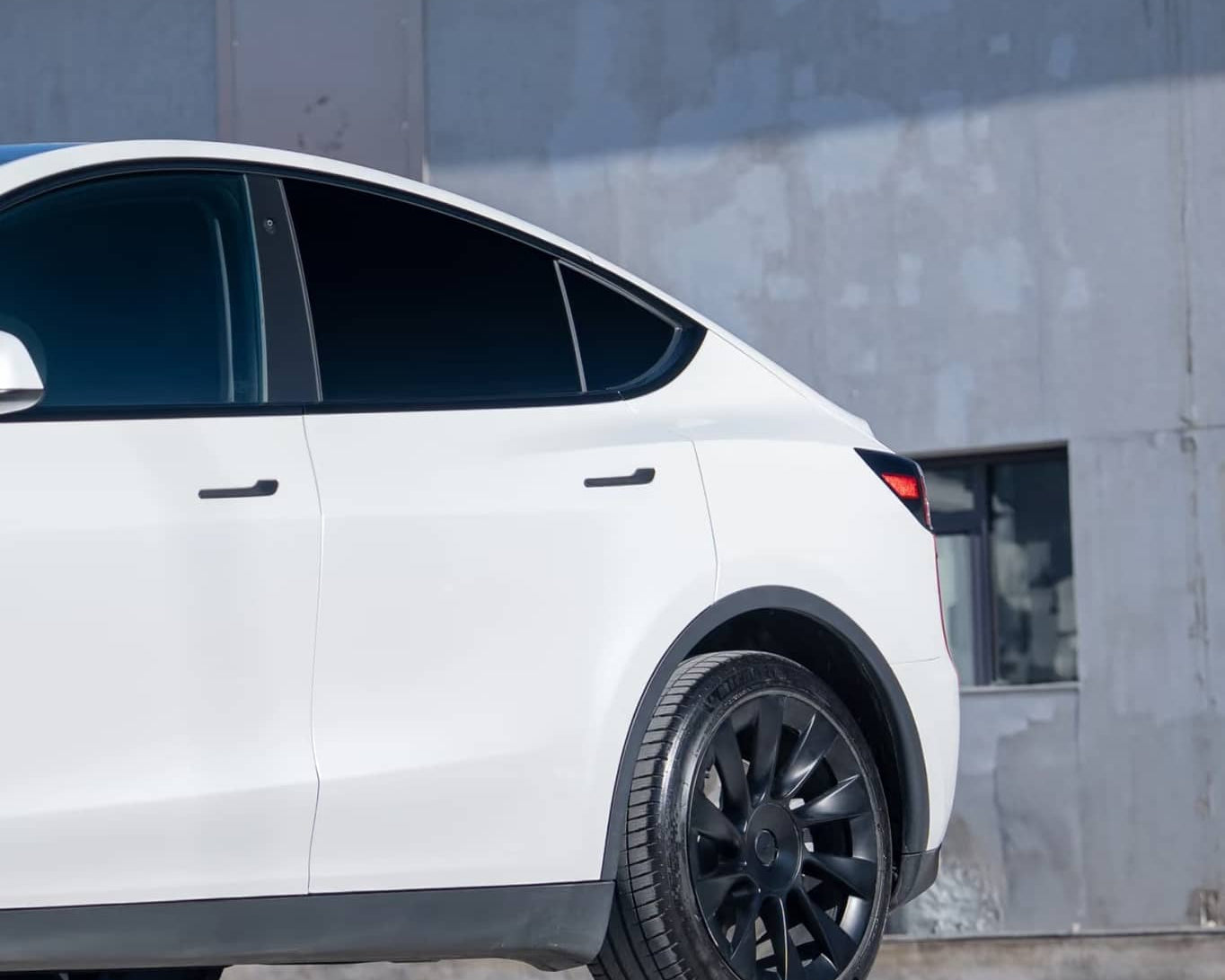 White Tesla Model Y with black wheels featuring a pre-cut Tesla wrap kit by WrapBug on a city street