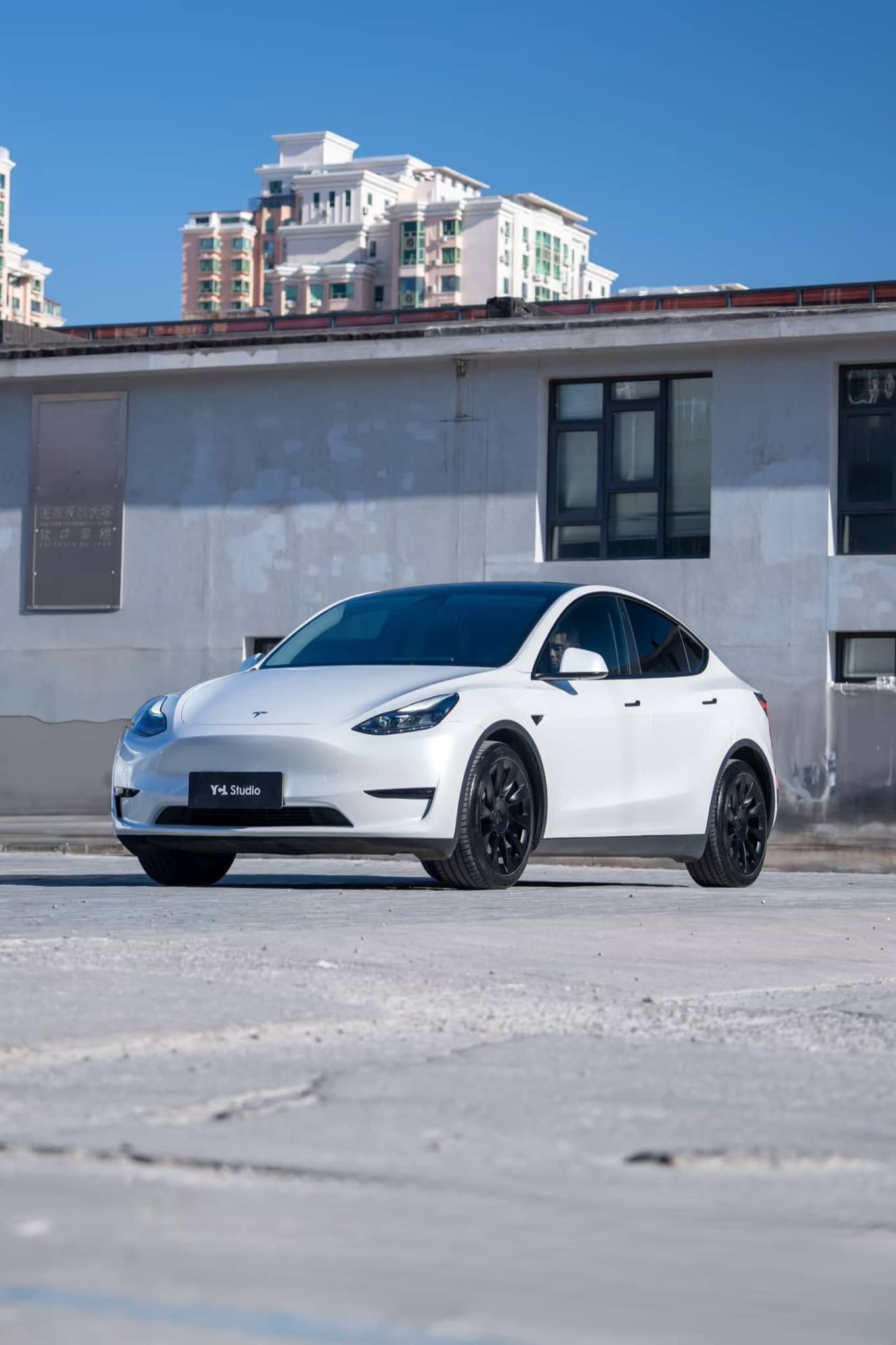 White Tesla Model Y with black wheels parked in urban area featuring Pre-cut Tesla Wrap Kit by WrapBug