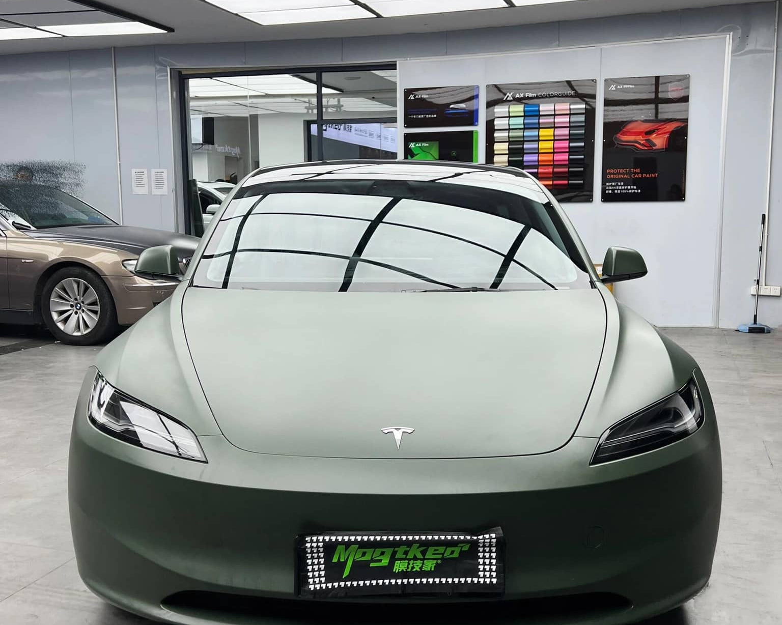 Front view of a Tesla car wrapped in matte OLIVE GREEN tesla wrap inside a modern showroom