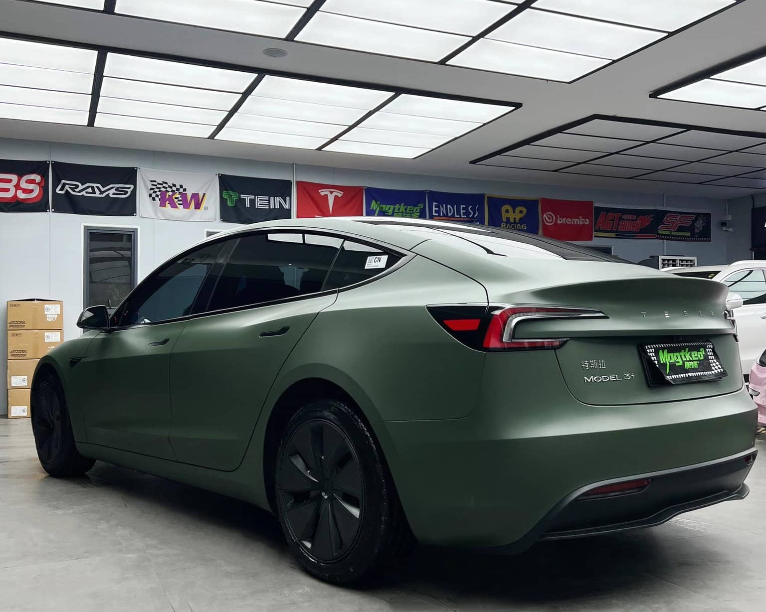 Matte olive green Tesla wrap on a sleek Tesla Model 3 parked inside a garage