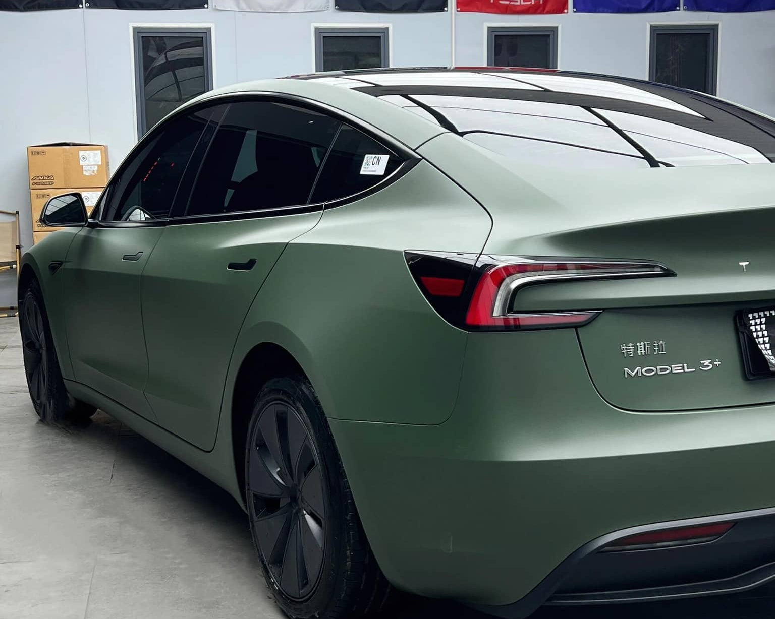 Tesla Model 3 with matte OLIVE GREEN tesla wrap by WrapBug parked indoors with branded banners