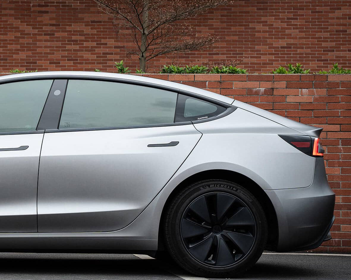 Silver Tesla Model 3 with matte finish parked beside brick wall featuring tesla model 3 wrap