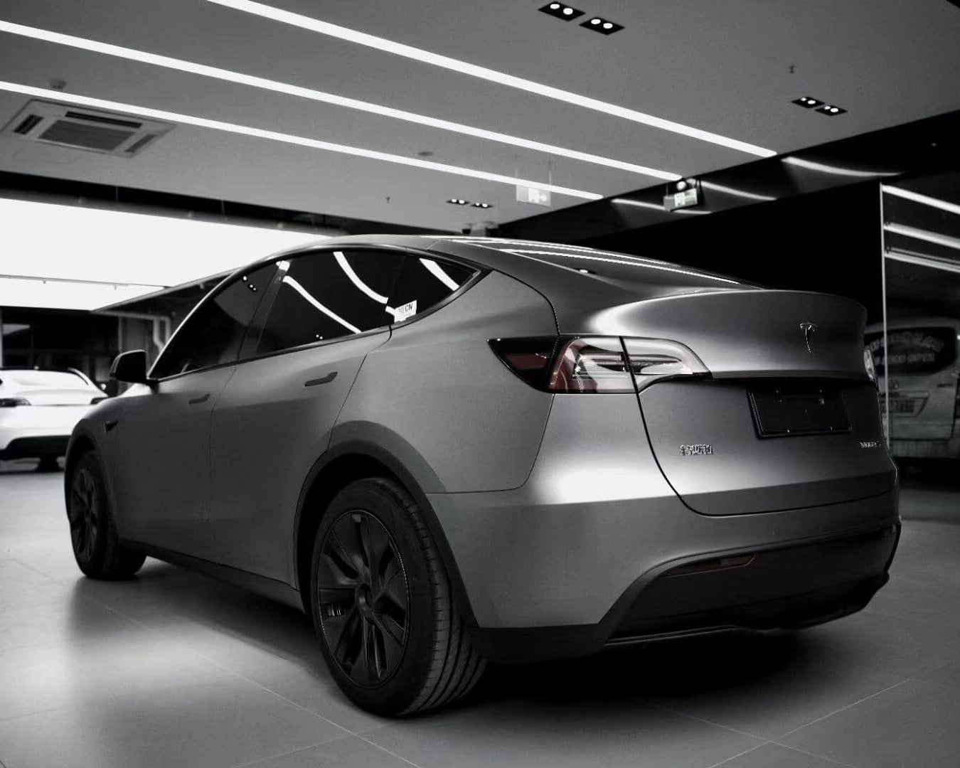 Tesla Model Y electric car in matte gray finish parked indoors under bright ceiling lights