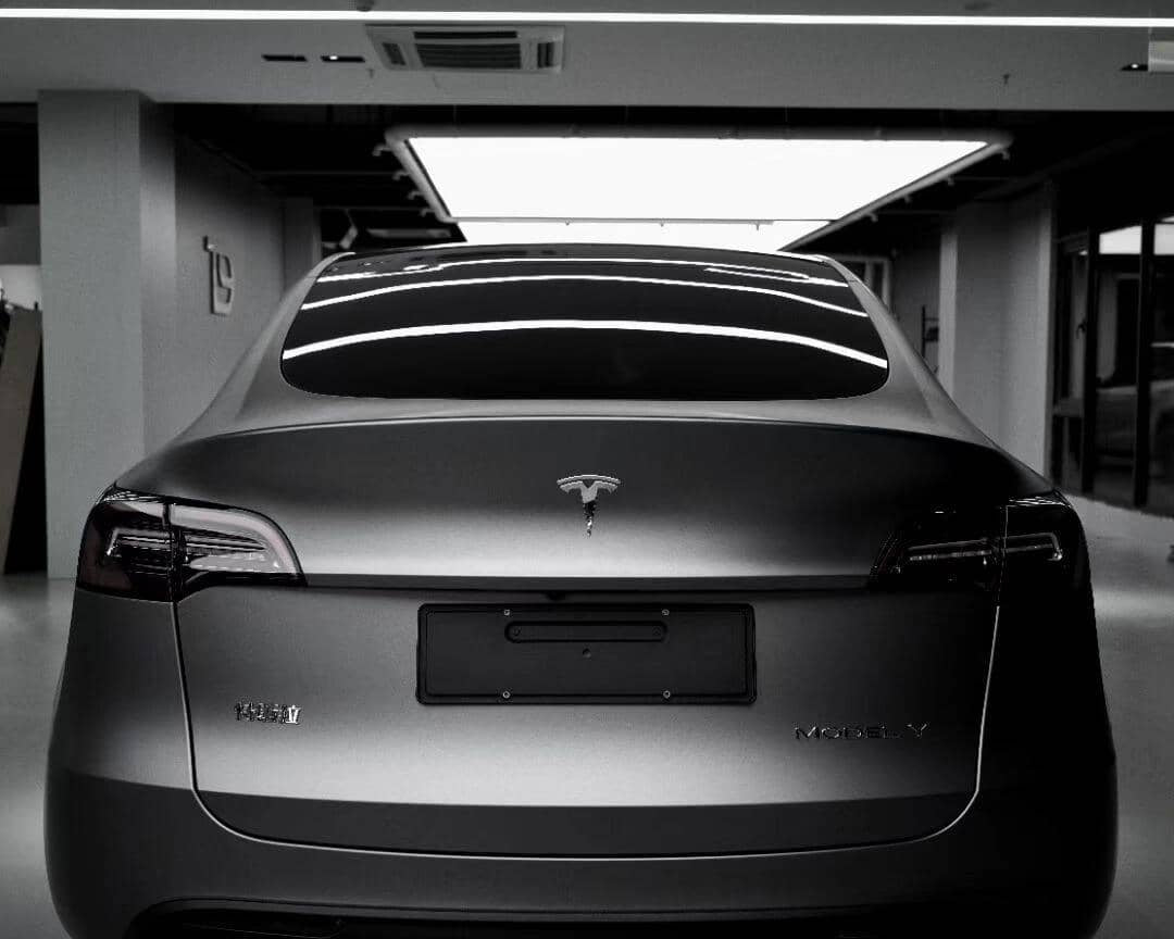 Rear view of a matte black Tesla Model X parked indoors under bright ceiling lights