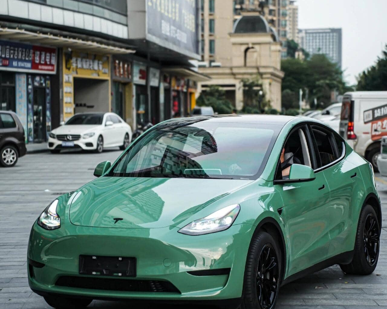 Tesla Model Y with green pre-cut Tesla vinyl wrap kit parked on city street by WrapBug