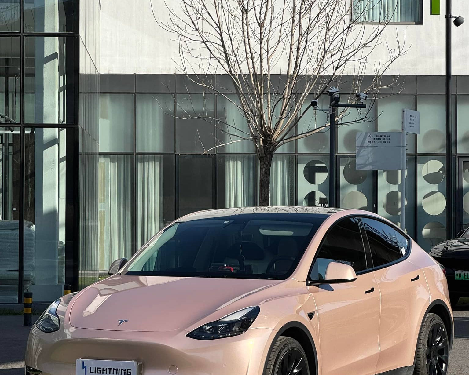 Pink Tesla Model Y wrapped using a Pre-cut Tesla Wrap Kit by WrapBug parked in front of a modern building