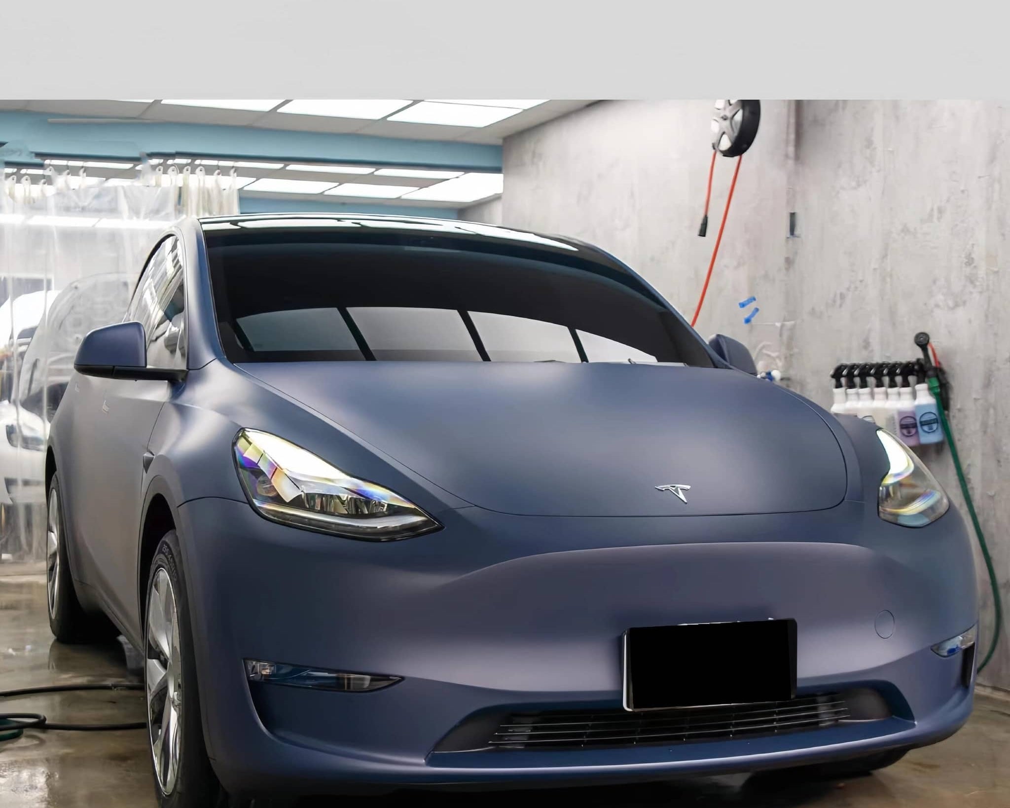 Matte blue Tesla with a smooth tesla vinyl wrap applied in a professional garage setting