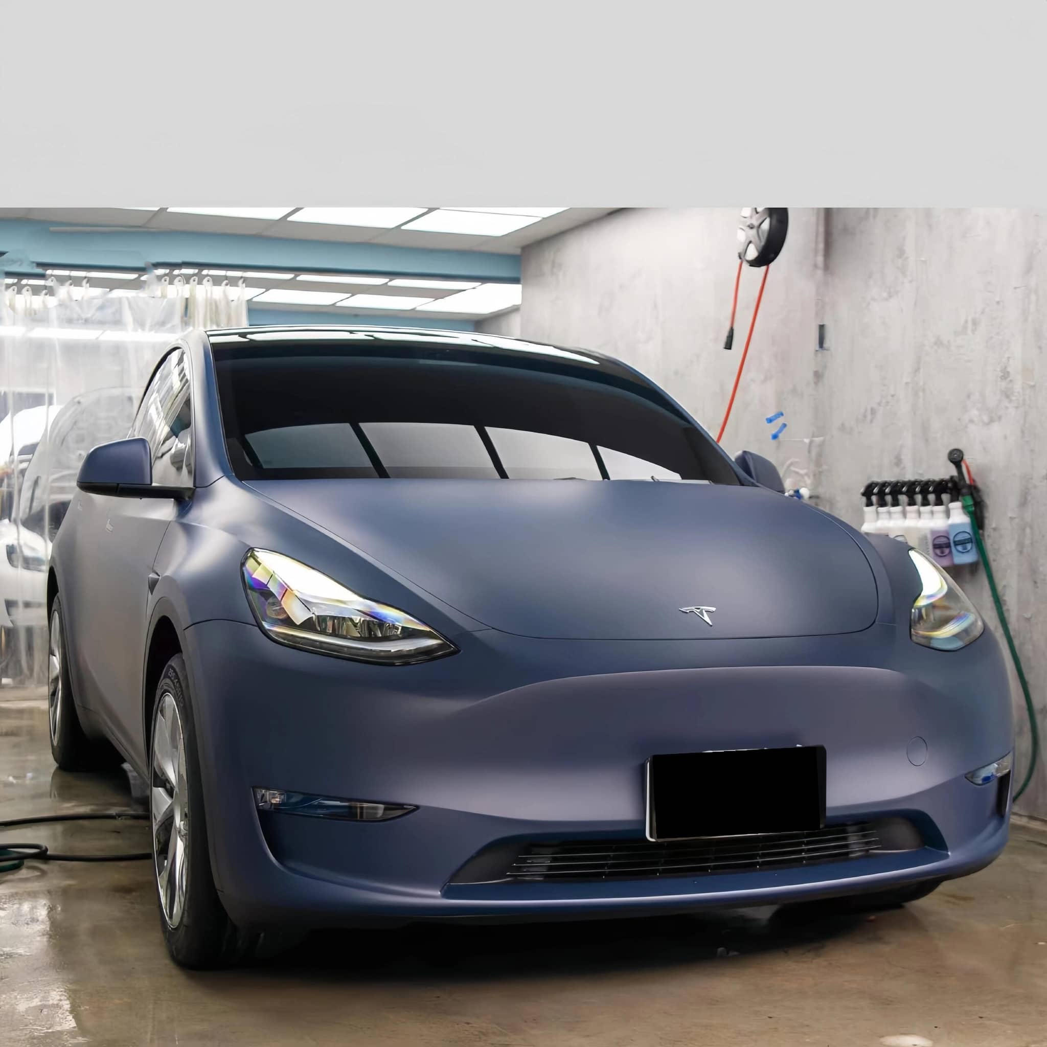 Matte blue Tesla with a smooth tesla vinyl wrap applied in a professional garage setting