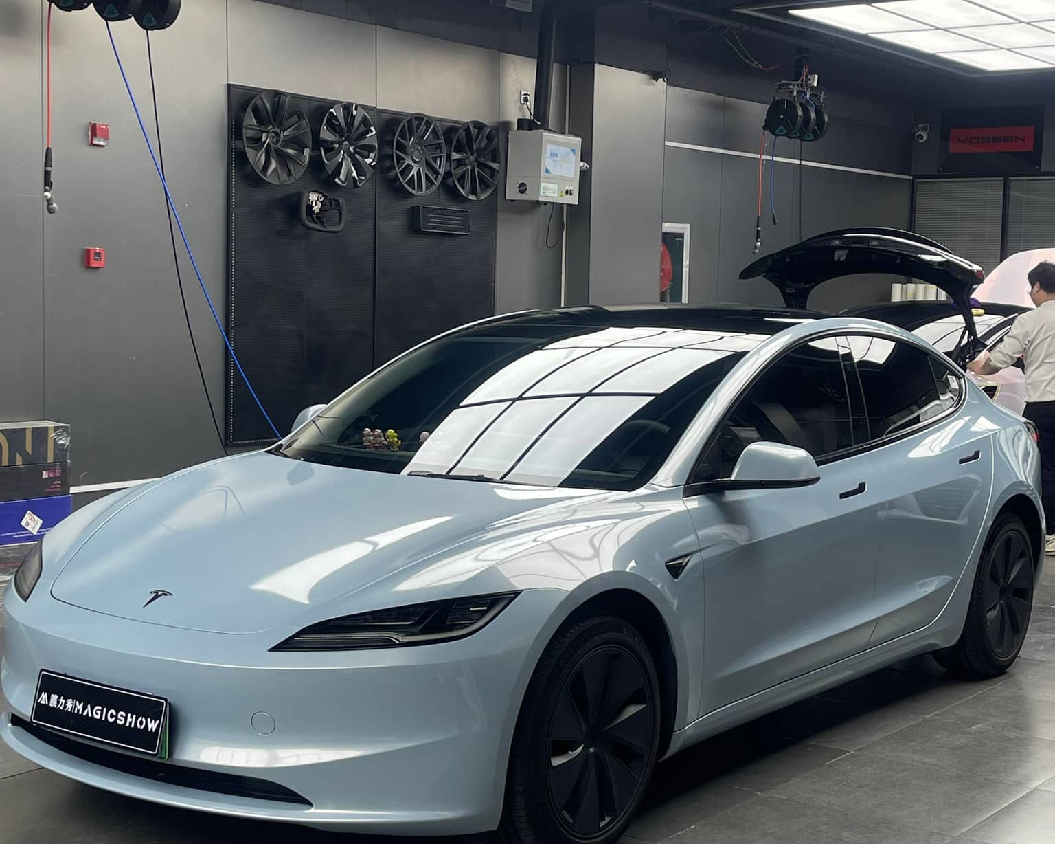 White Tesla Model 3 parked in a garage with reflective ceiling lights and black alloy wheels