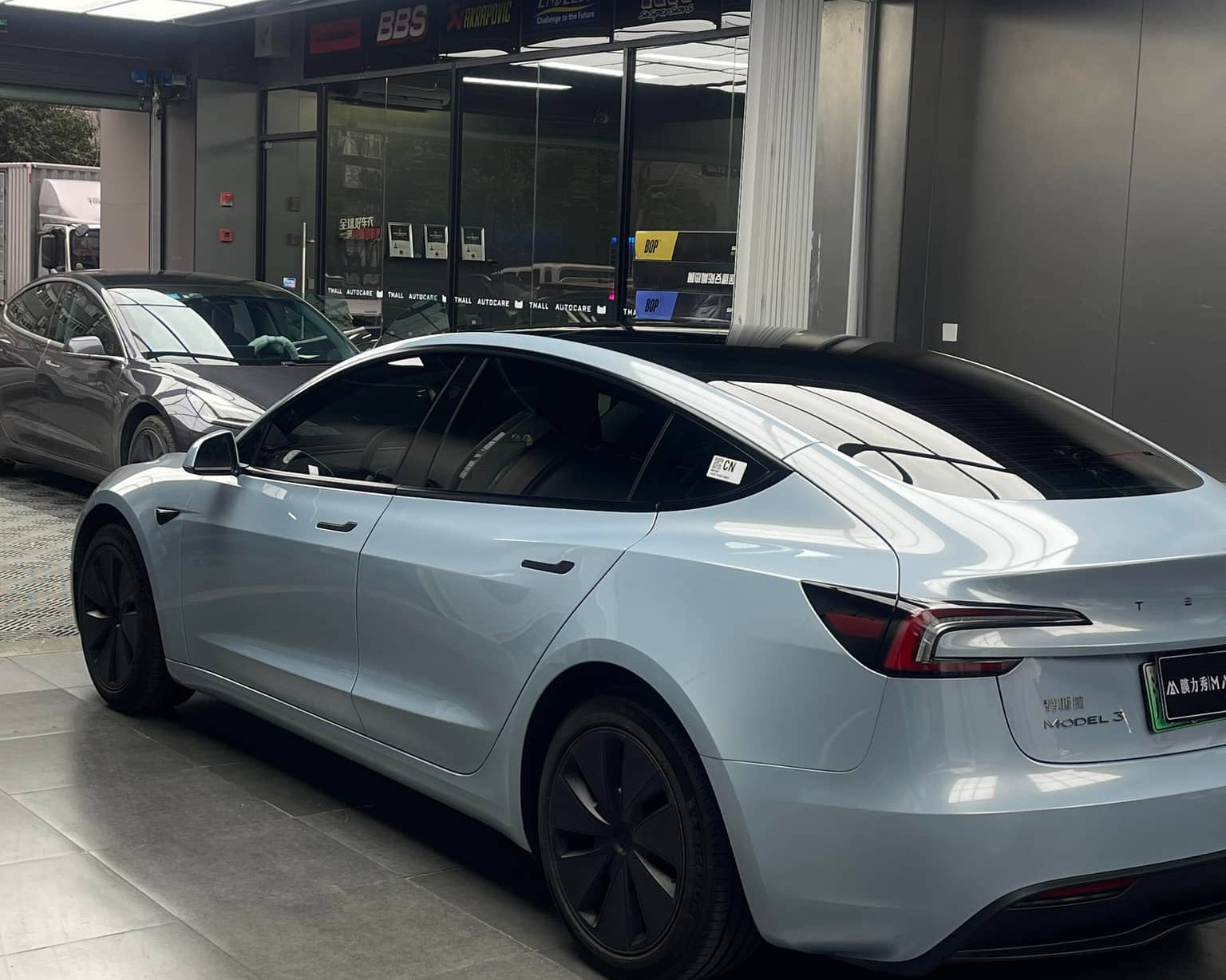 Silver Tesla Model 3 electric car parked indoors with tinted windows and black wheel covers