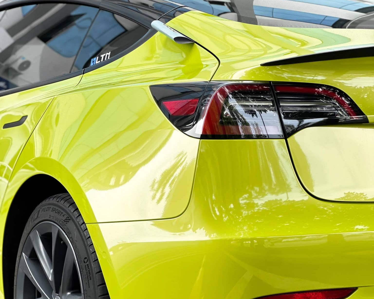 Bright yellow Tesla Model 3 wrapped with pre-cut Tesla vinyl wrap kit by WrapBug showing rear side view