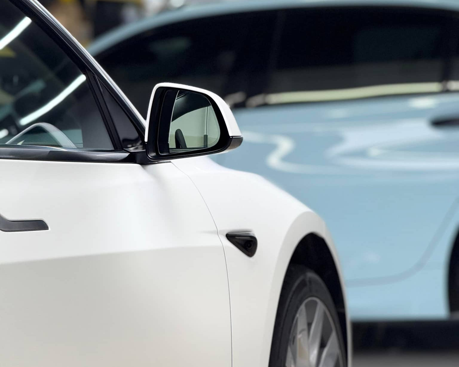 White Tesla with Pre-cut Tesla Vinyl Wrap Kit applied, focusing on side mirror and front wheel in a garage
