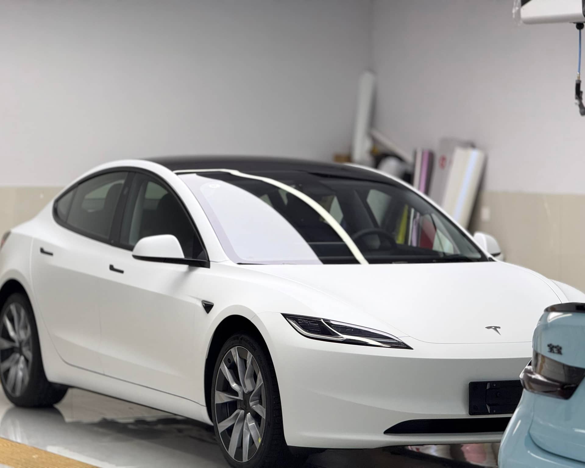 White Tesla Model 3 in garage showcasing a Pre-cut Tesla Vinyl Wrap Kit by WrapBug