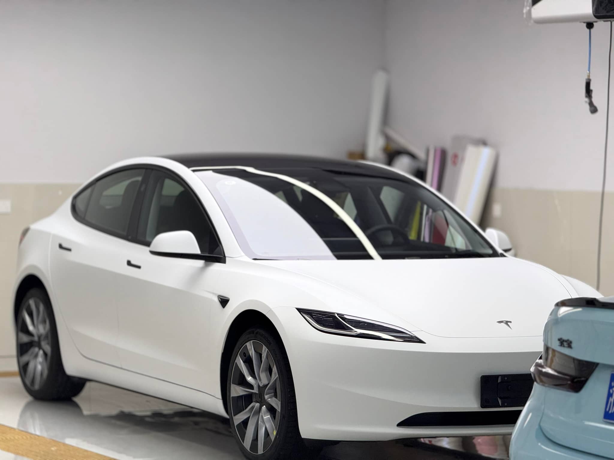 White Tesla Model 3 in garage showcasing a Pre-cut Tesla Vinyl Wrap Kit by WrapBug