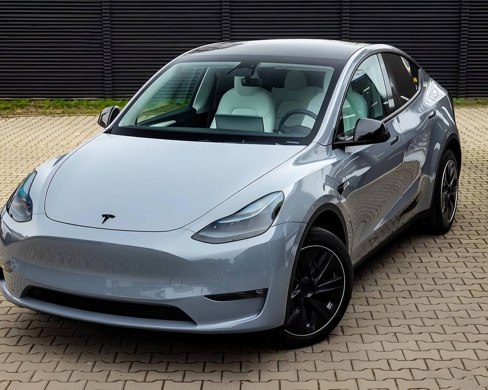 Silver Tesla Model Y electric SUV parked on tiled ground with black alloy wheels