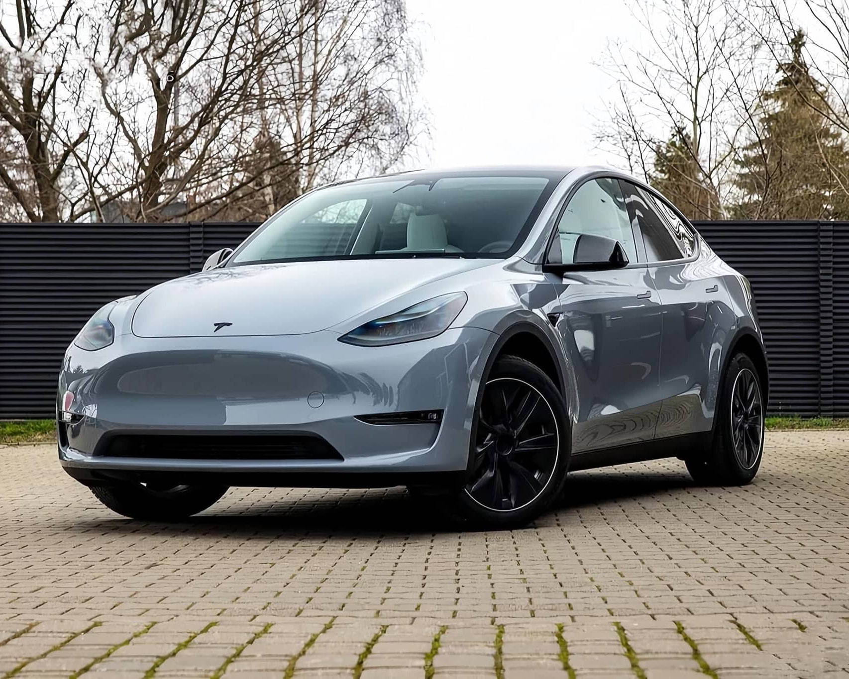 Silver Tesla Model Y electric SUV parked on a paved driveway with black wheels