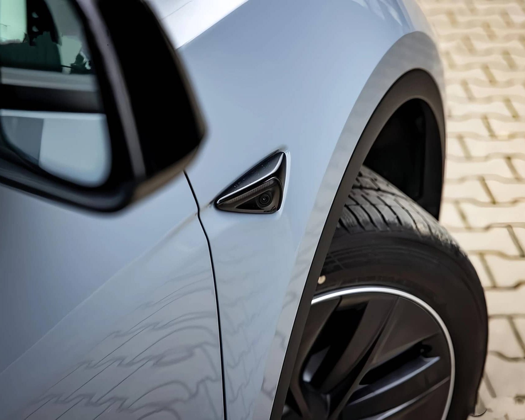Close-up of light blue car's front wheel and side mirror with WrapBug paint protection film applied
