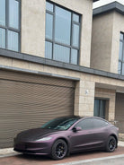 WrapBug matte purple Tesla Model 3 parked in front of a modern garage with black rims