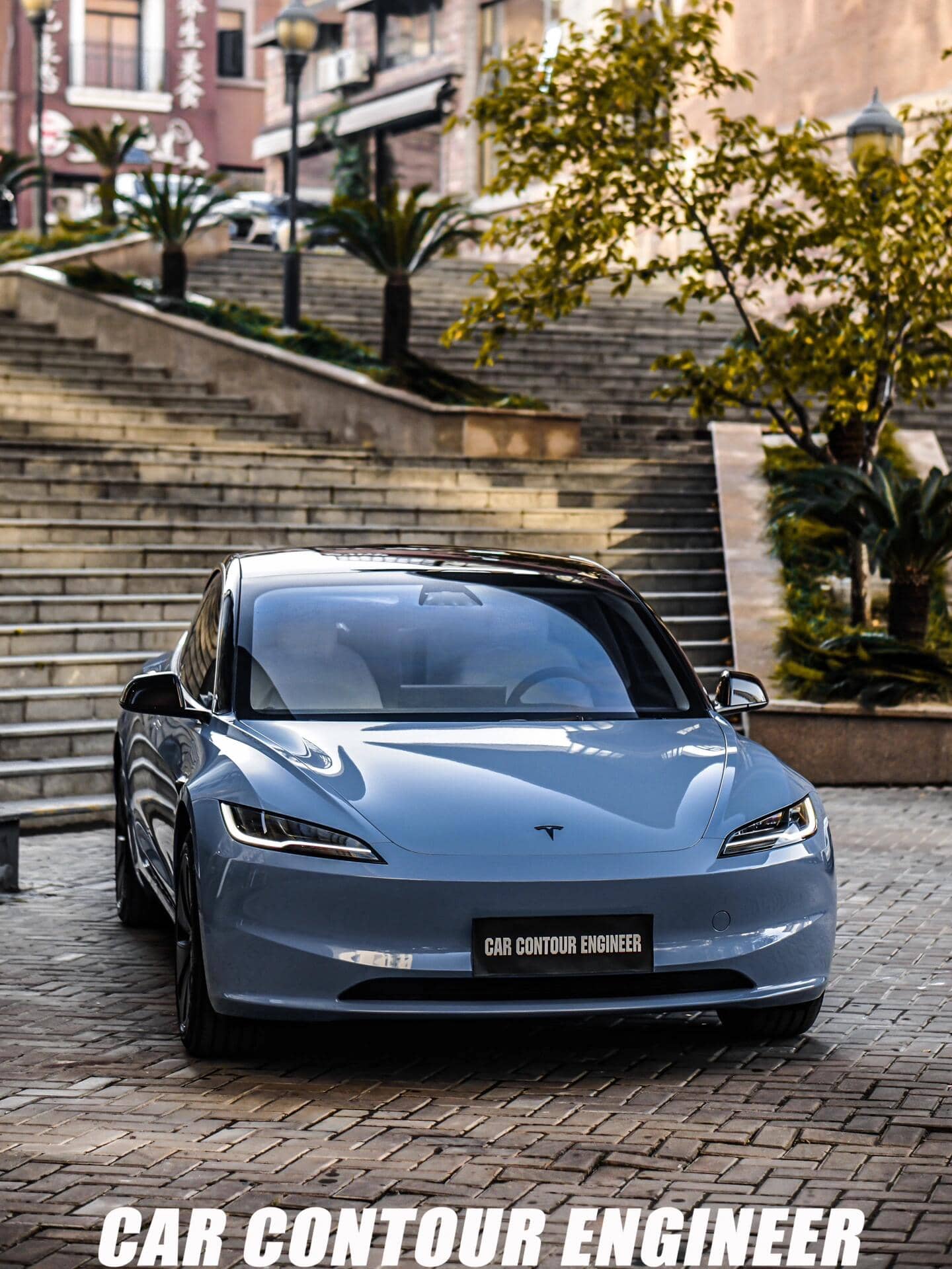 Pre-cut Tesla Vinyl Wrap Kit applied on sleek blue Tesla parked near stone stairs and greenery