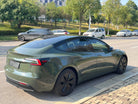 Green Tesla Model 3 electric car parked on street with black wheel covers under clear sky