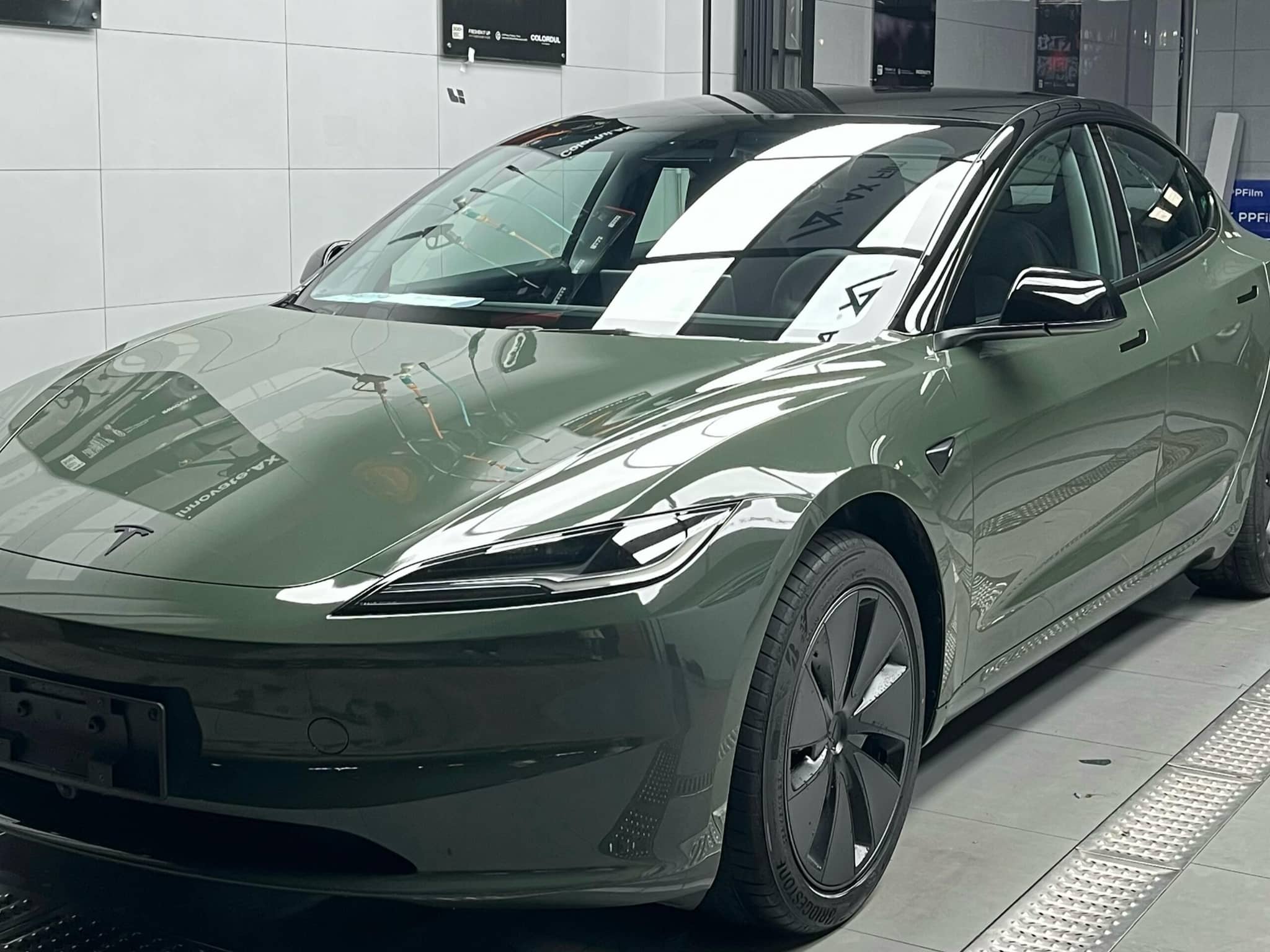 Green matte finish Tesla Model 3 electric car parked indoors with sleek aerodynamic design