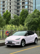 WrapBug pink Tesla Model Y electric car parked on city street near greenery and buildings