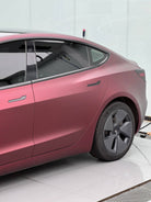 WrapBug matte burgundy car wrap on a Tesla Model 3 parked indoors with black rims