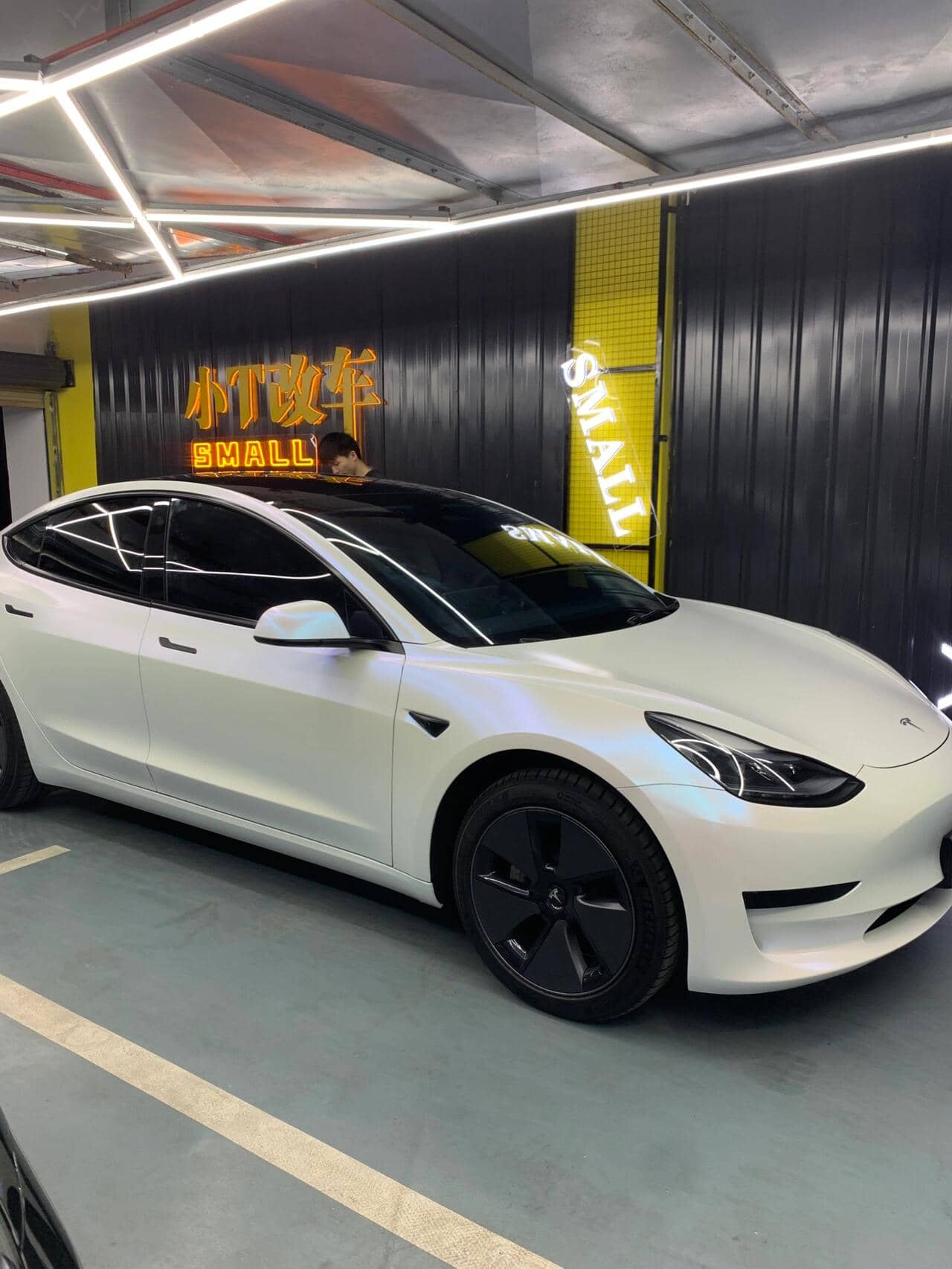 White Tesla Model 3 with matte white tesla wrap parked indoors under bright lighting