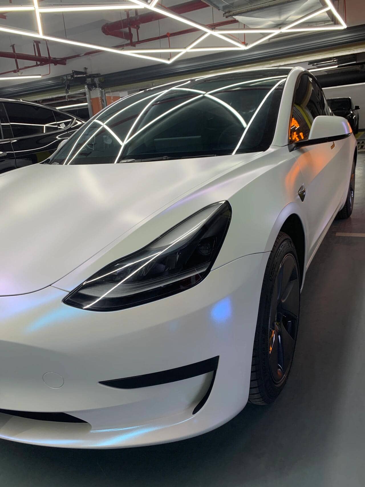 Tesla Model 3 with sleek matte white tesla wrap by WrapBug in a modern garage setting